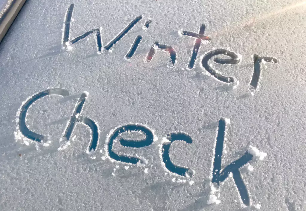 Handgeschriebener Schriftzug "Winter Check" im Frost auf einer Autoscheibe, Hinweis auf wichtige Winterfahrzeug-Sicherheit.