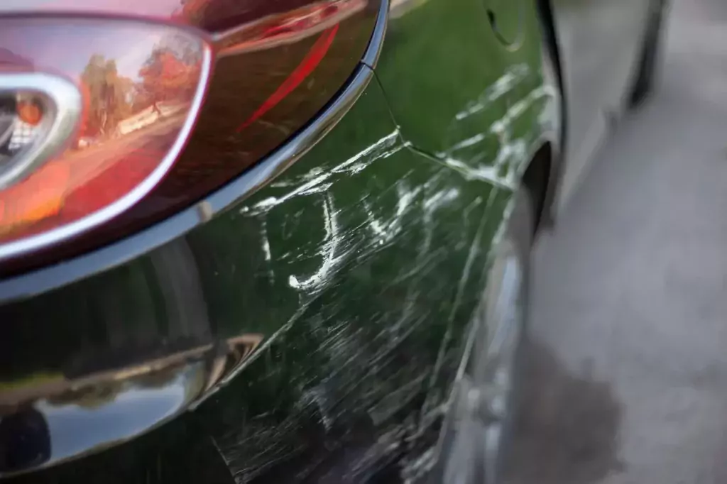 Schwarzes Auto in Nahaufnahme mit weißen Kratzern und Schrammen in der Nähe des hinteren Rücklichts, das leichte Lackschäden von einer Schramme aufweist.