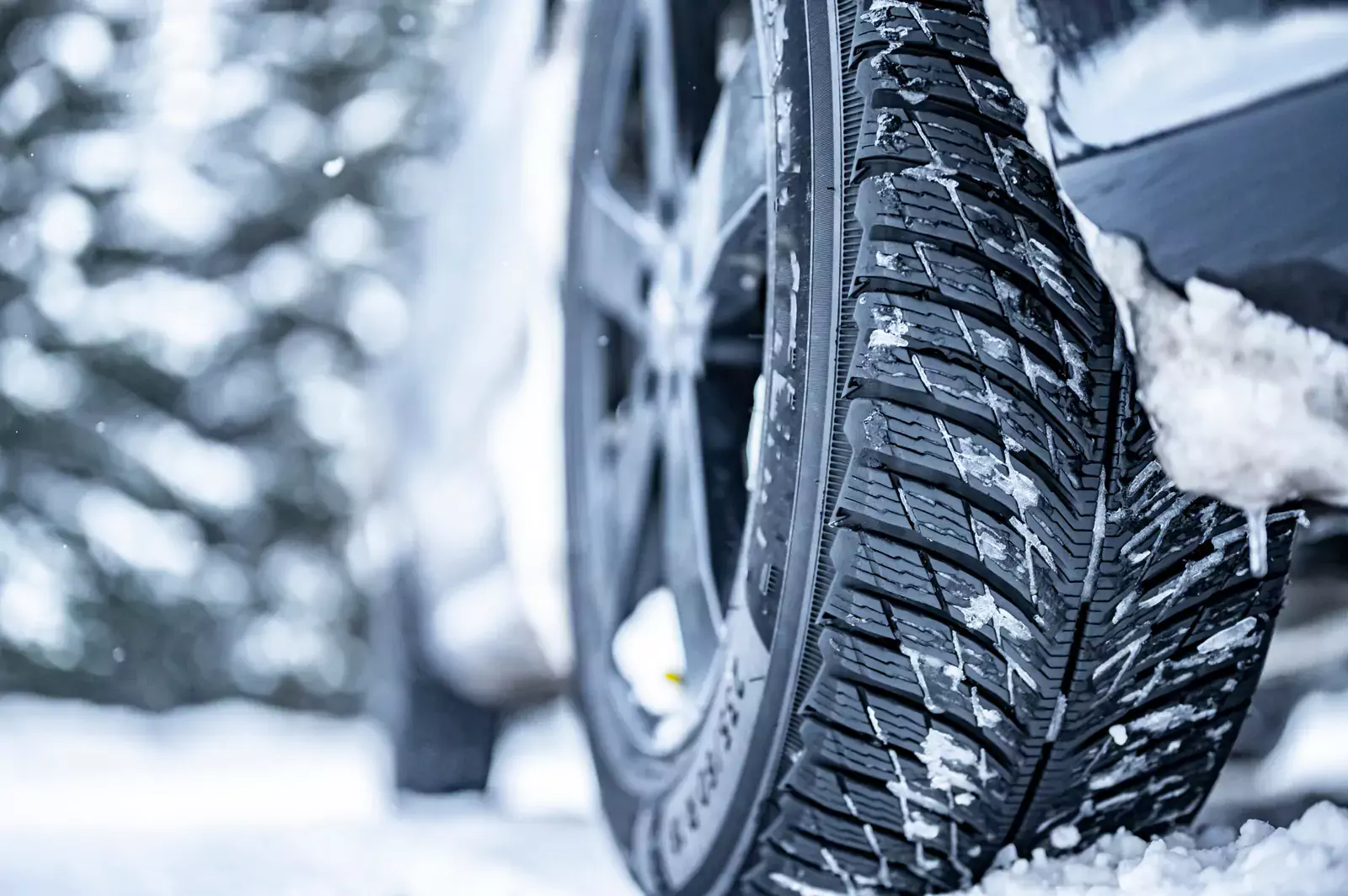 Nahaufnahme eines Autoreifens mit Schnee, betont sicheres Fahren im Winter; verschneite Oberfläche und unscharfer Hintergrund.