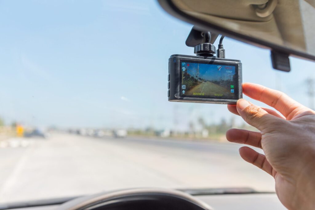 Hand justiert Dashcam an Autoscheibe, nimmt eine freie Straße bei sonnigem Wetter auf.