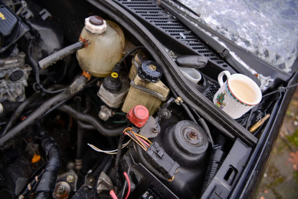 Ein Keramikbecher mit Tee oder Kaffee steht auf einem Motorraum, umgeben von Motorteilen und Kabeln.