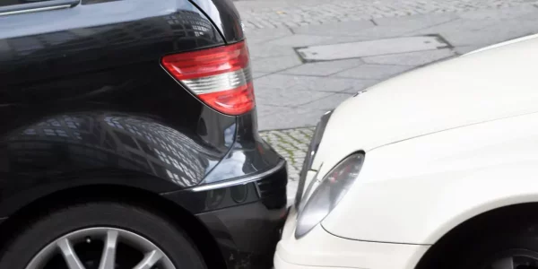 Die vordere Stoßstange eines weißen Autos berührt das Heck eines schwarzen Autos, was wie ein kleiner Unfall auf einer Stadtstraße aussieht.